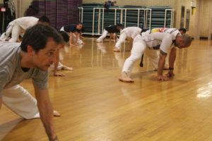 A group of people stretching, balancing with their legs spread wide, leaning on their hands. 