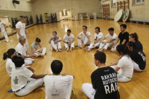 A group of students sit in a circle, listening the wisdom of a capoeira master.